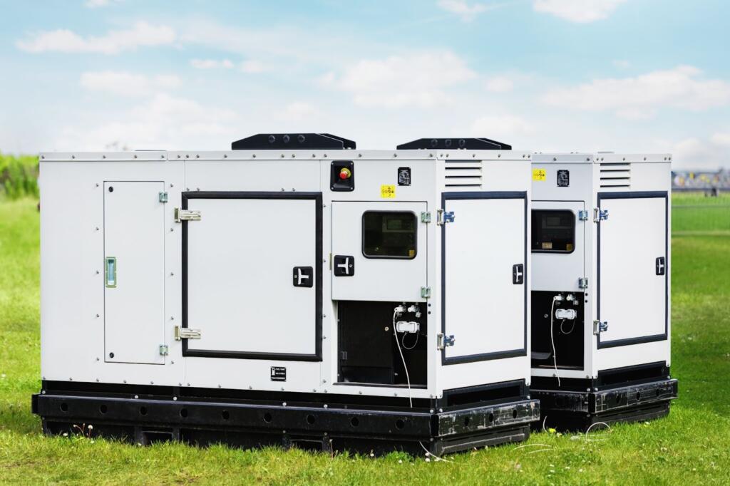 Two large generators are on a green lawn.