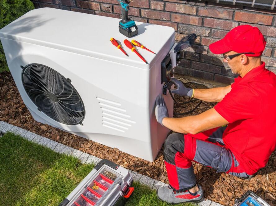 HVAC technician in red and gray uniform installing a residential heat pump unit outdoors
