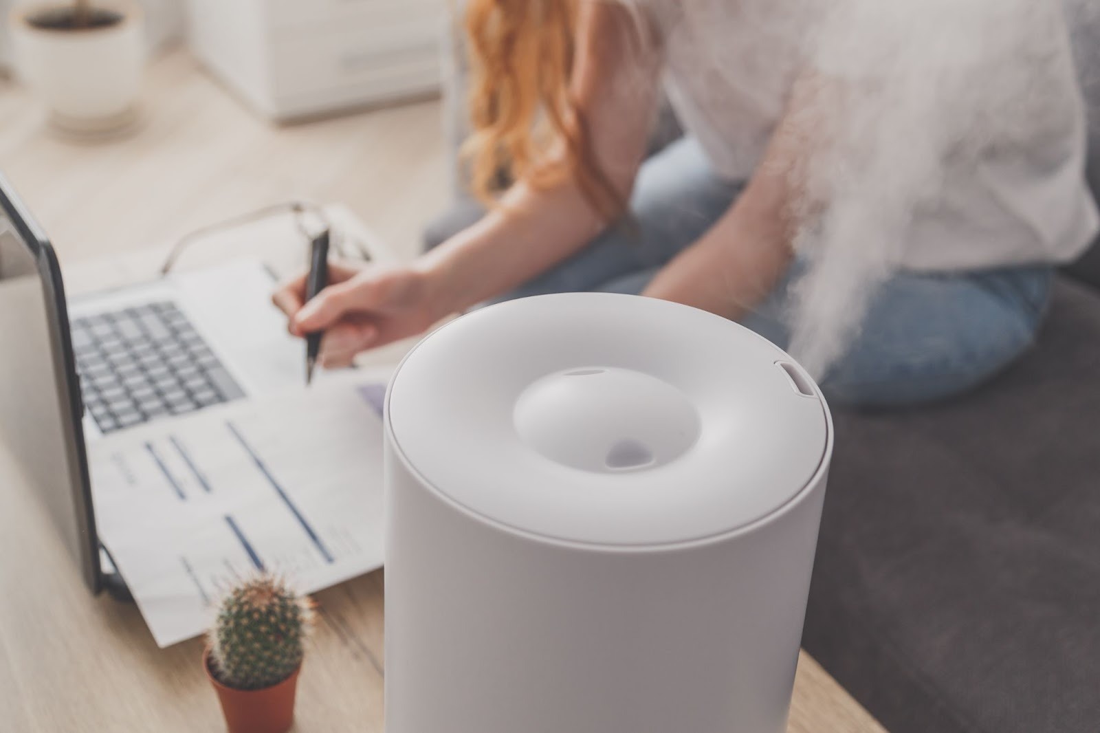 A woman is working on her laptop next to a humidifier.