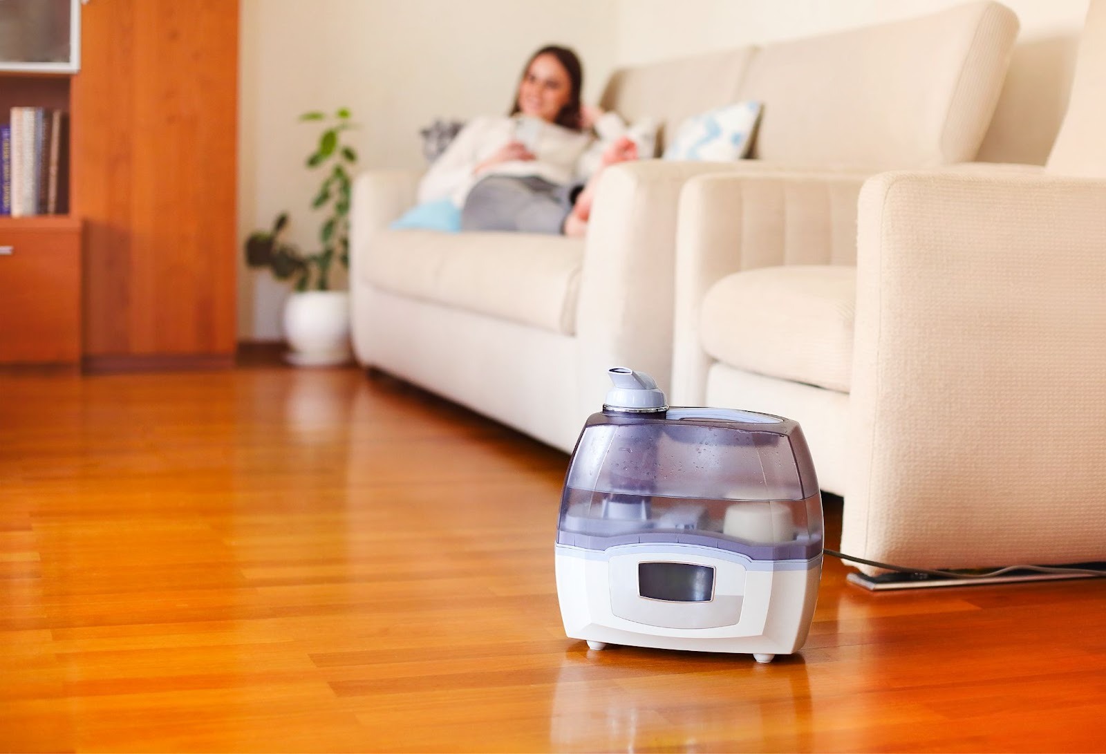 A humidifier running in a living room while a woman relaxes on the sofa